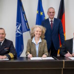 Rüstungsbeschaffung der Zukunft: Staatssekretär Zimmer (stehend), Vizeadmiral Stawitzki (l.), Prof. Kern (m.) und Vizepräsident des BAAINBw Herzog (r.) bei der Unterzeichnung